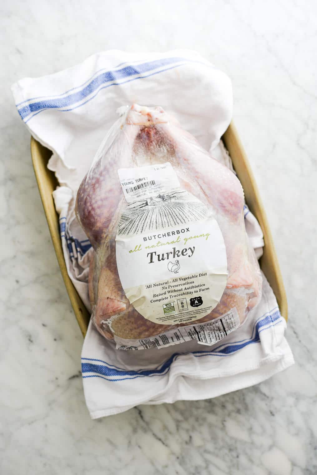 top view of a raw frozen turkey (still in packaging) thawing in a dish towel lined roasting pan