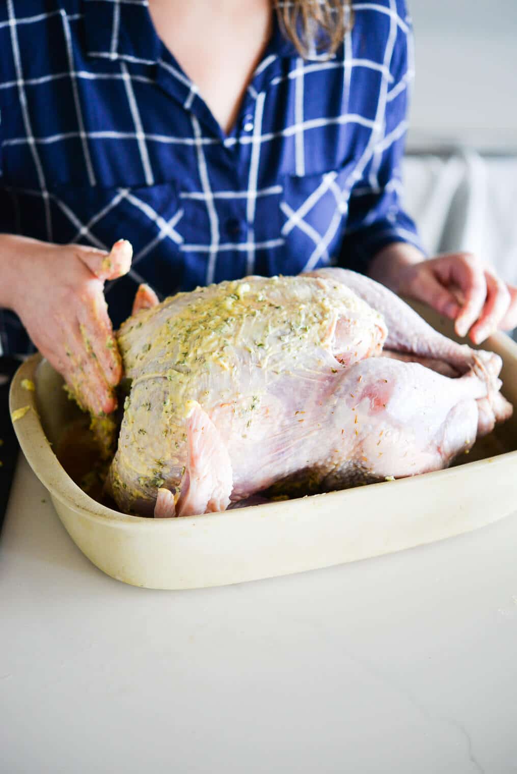 side view of a raw whole turkey being rubbed with herb butter