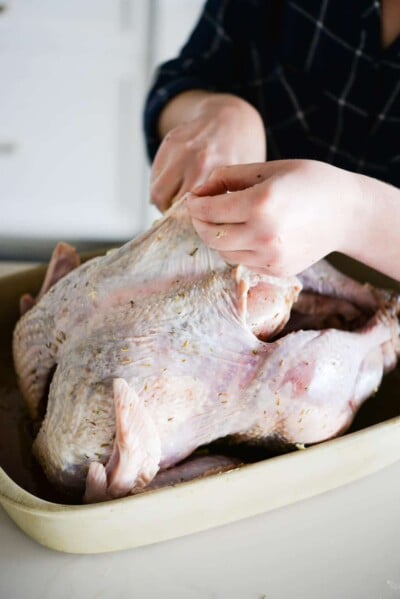 a raw whole turkey being rubbed with herbs and butter