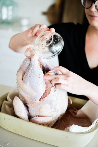 a raw whole turkey being rubbed with butter and herbs