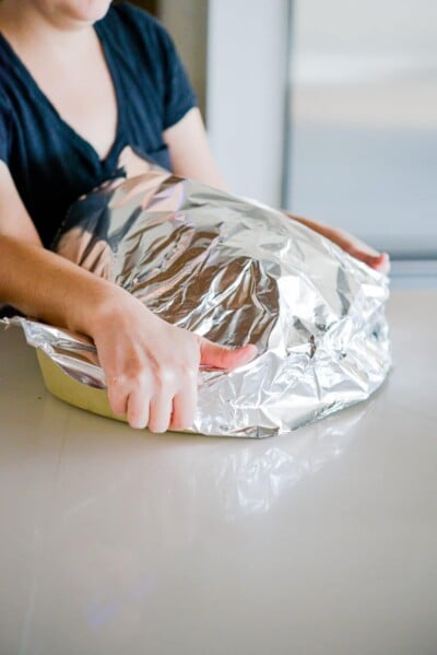 a whole roasted turkey being covered with aluminum foil