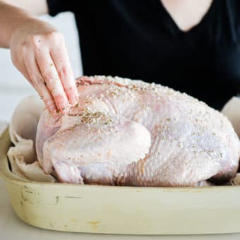 a raw whole turkey being rubbed with butter and herbs