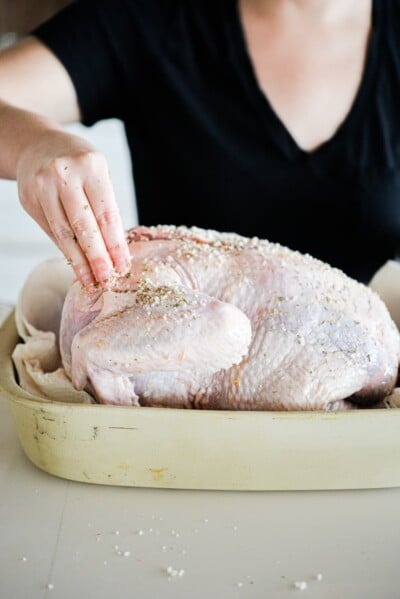 a raw whole turkey being rubbed with butter and herbs