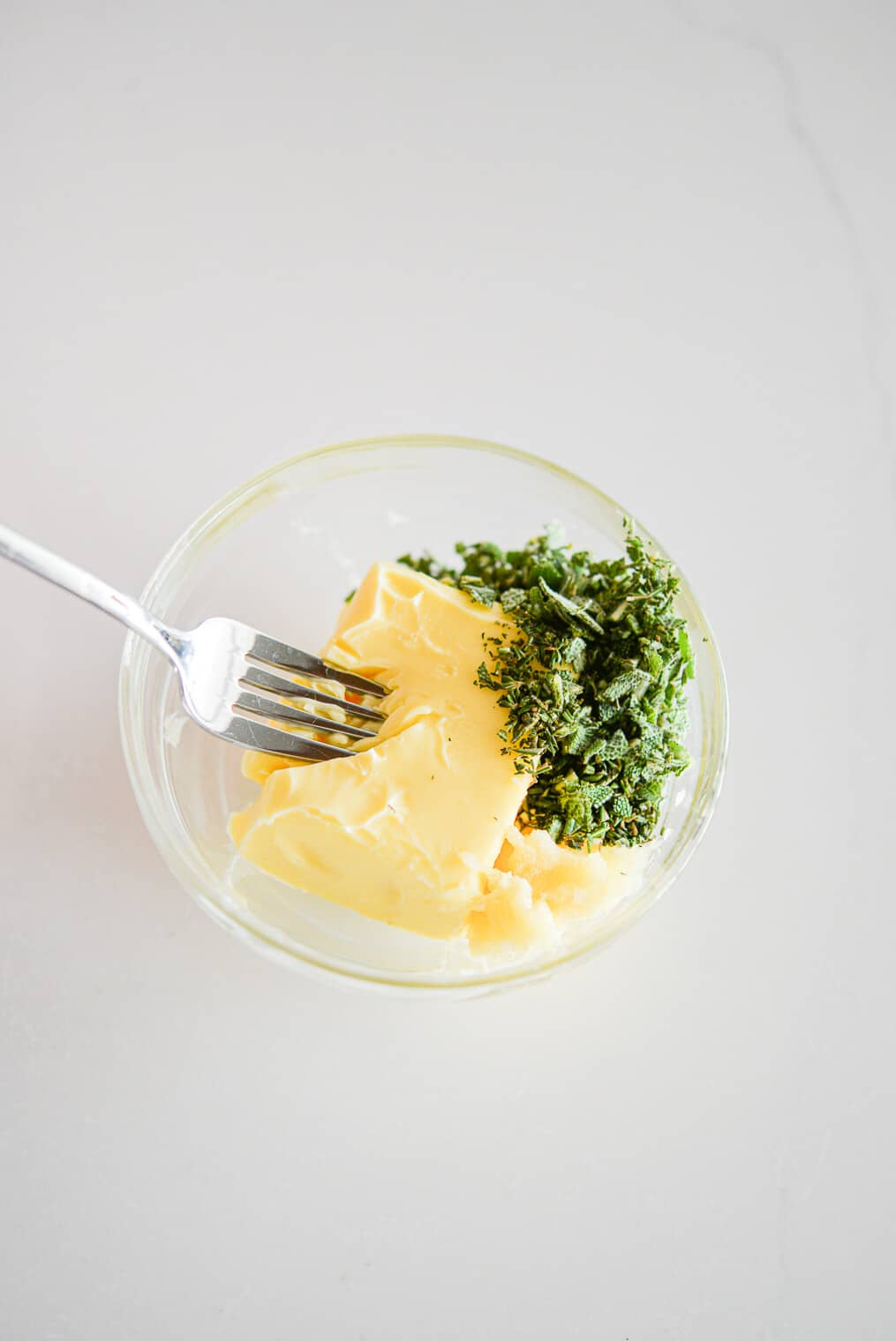 top view of a small glass bowl of butter and herbs to make herb butter rub