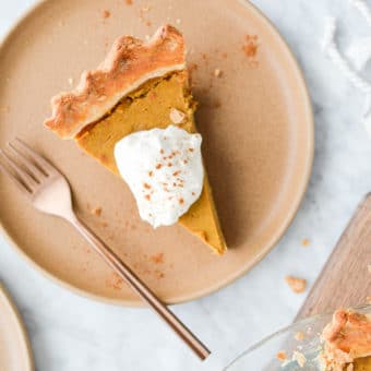 close up top view of a slice of pumpkin pie with whipped cream on top sitting on a plate