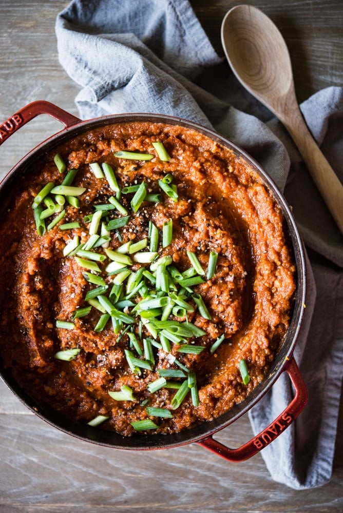 a large red dutch oven filled with a deep orange pumpkin chili topped with sliced green onions