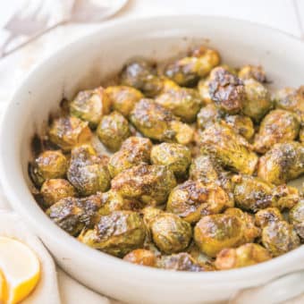 whole roasted brussels sprouts in a round, white ceramic dish on top of a linen towel