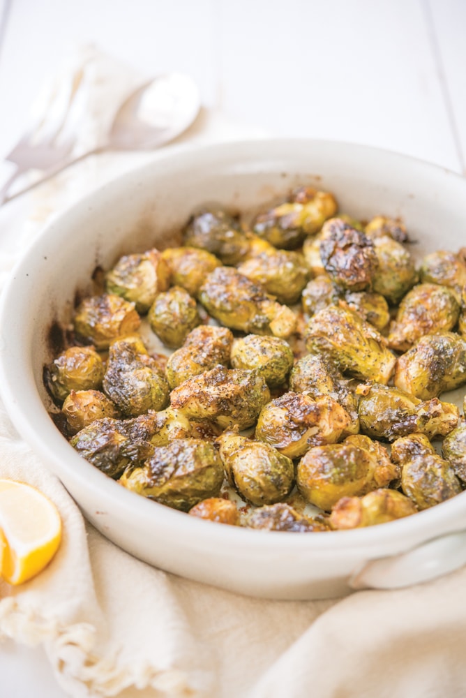 whole roasted brussels sprouts in a round, white ceramic dish on top of a linen towel