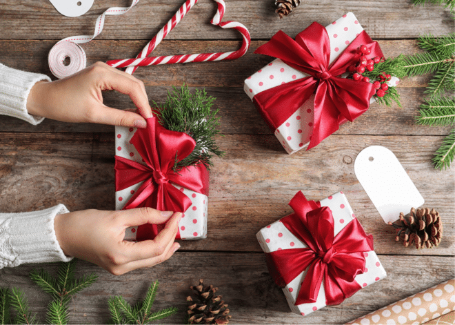 woman's hands wrapping a present with white and red polka dot wrapping and a red bow on a wooden surface