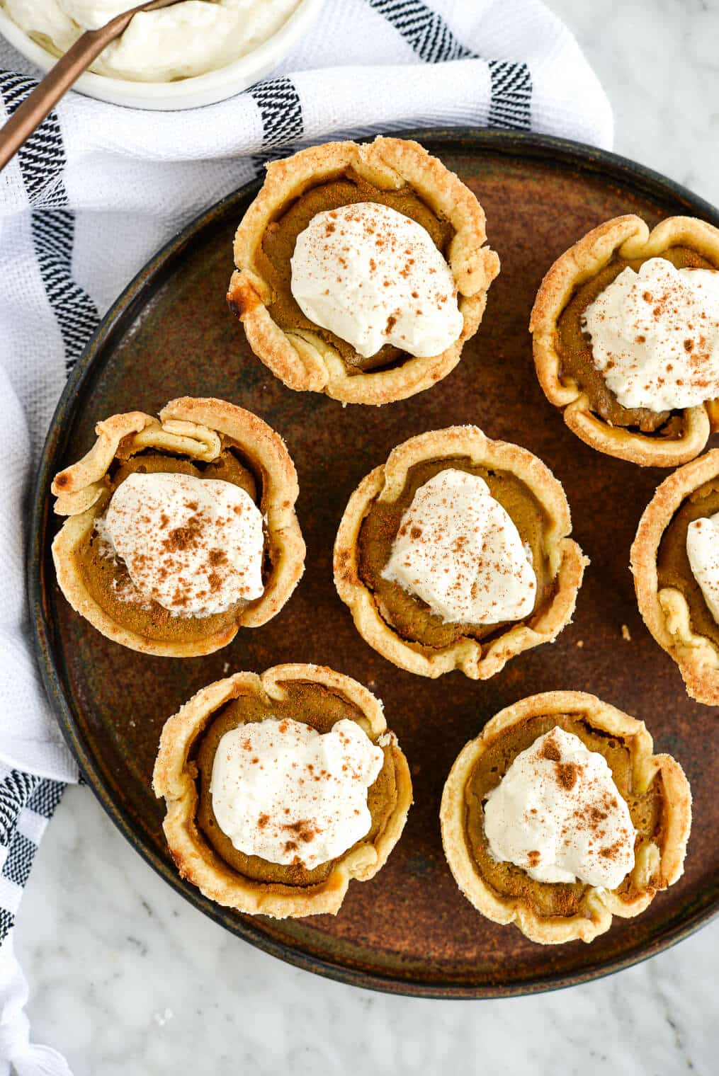 the top view of a plate of mini pumpkin pies topped with homemade whipped cream