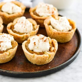 the side view of a plate of mini pumpkin pies topped with homemade whipped cream