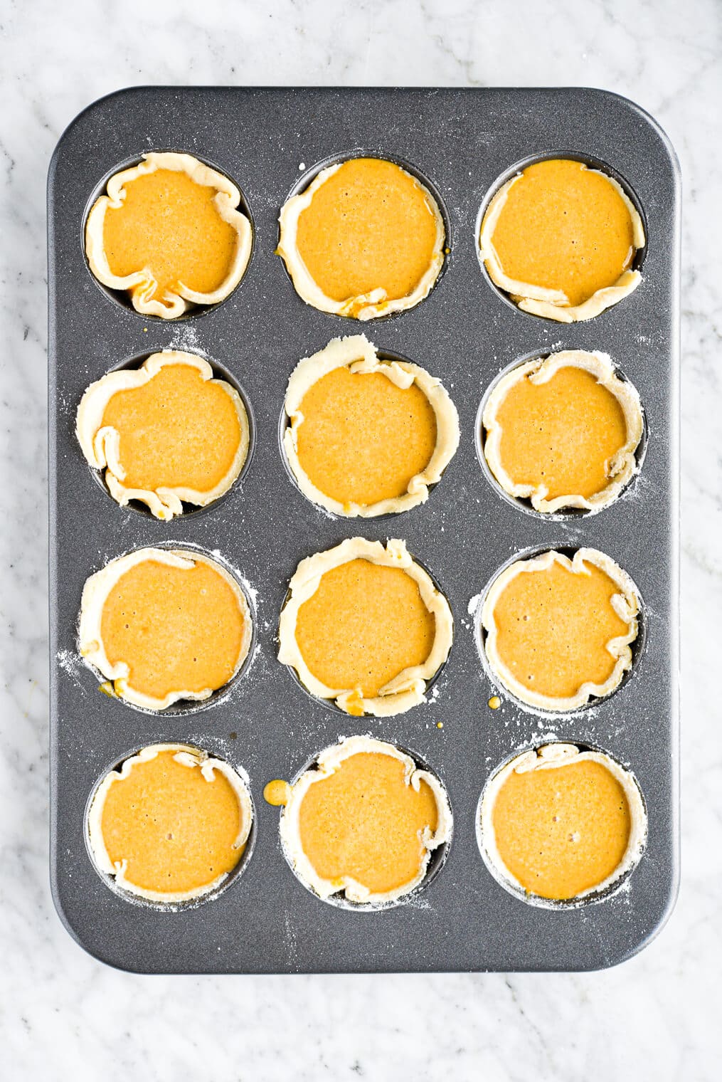 12 mini pumpkin pies filling up a muffin tin and ready to go into the oven