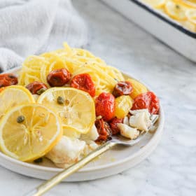 the side view of a plate of lemon garlic baked cod, roasted tomatoes, and garlic parmesan pasta