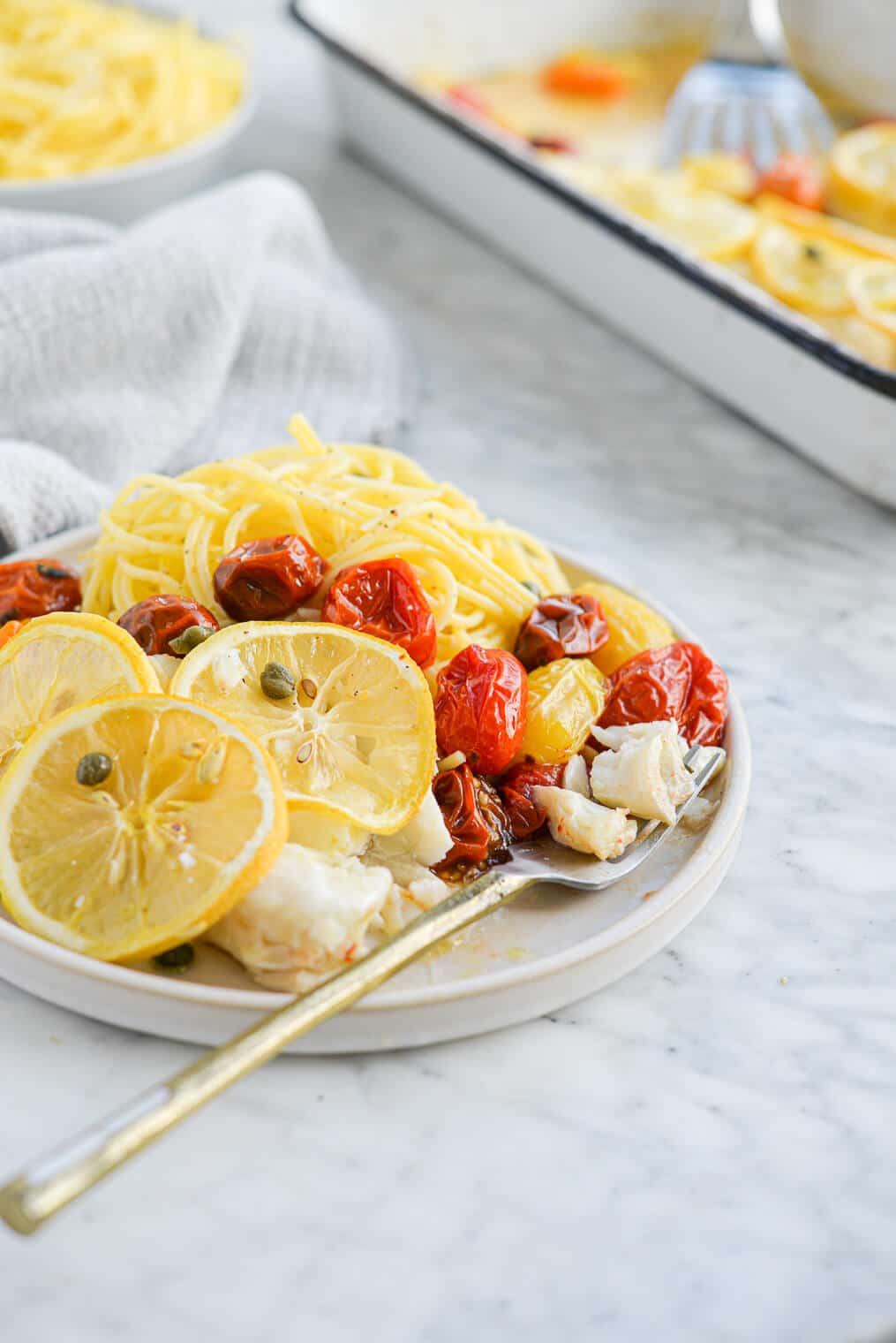 the side view of a plate of lemon garlic baked cod, roasted tomatoes, and garlic parmesan pasta