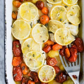 the top view of a roasting dish of baked cod topped with thin sliced lemons and roasted tomatoes