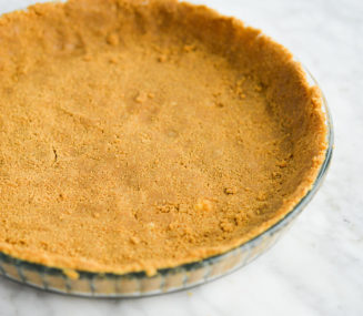 a graham cracker crust pressed into a clear glass pie plate sitting on a marble surface