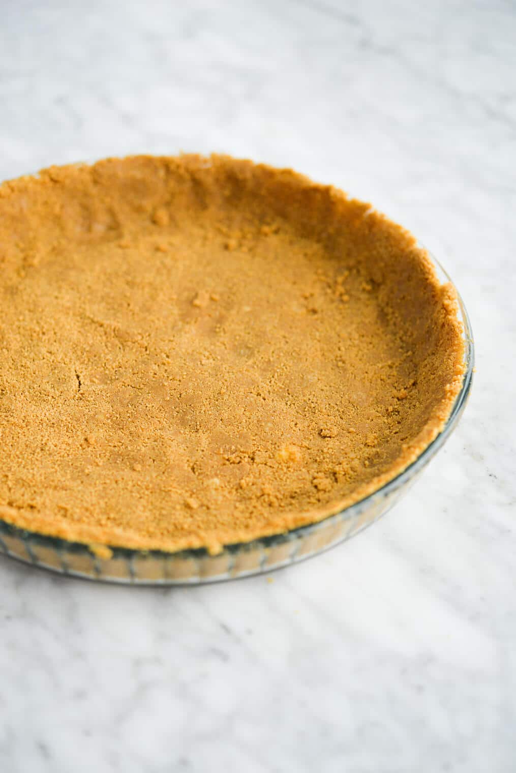 a graham cracker crust pressed into a clear glass pie plate sitting on a marble surface