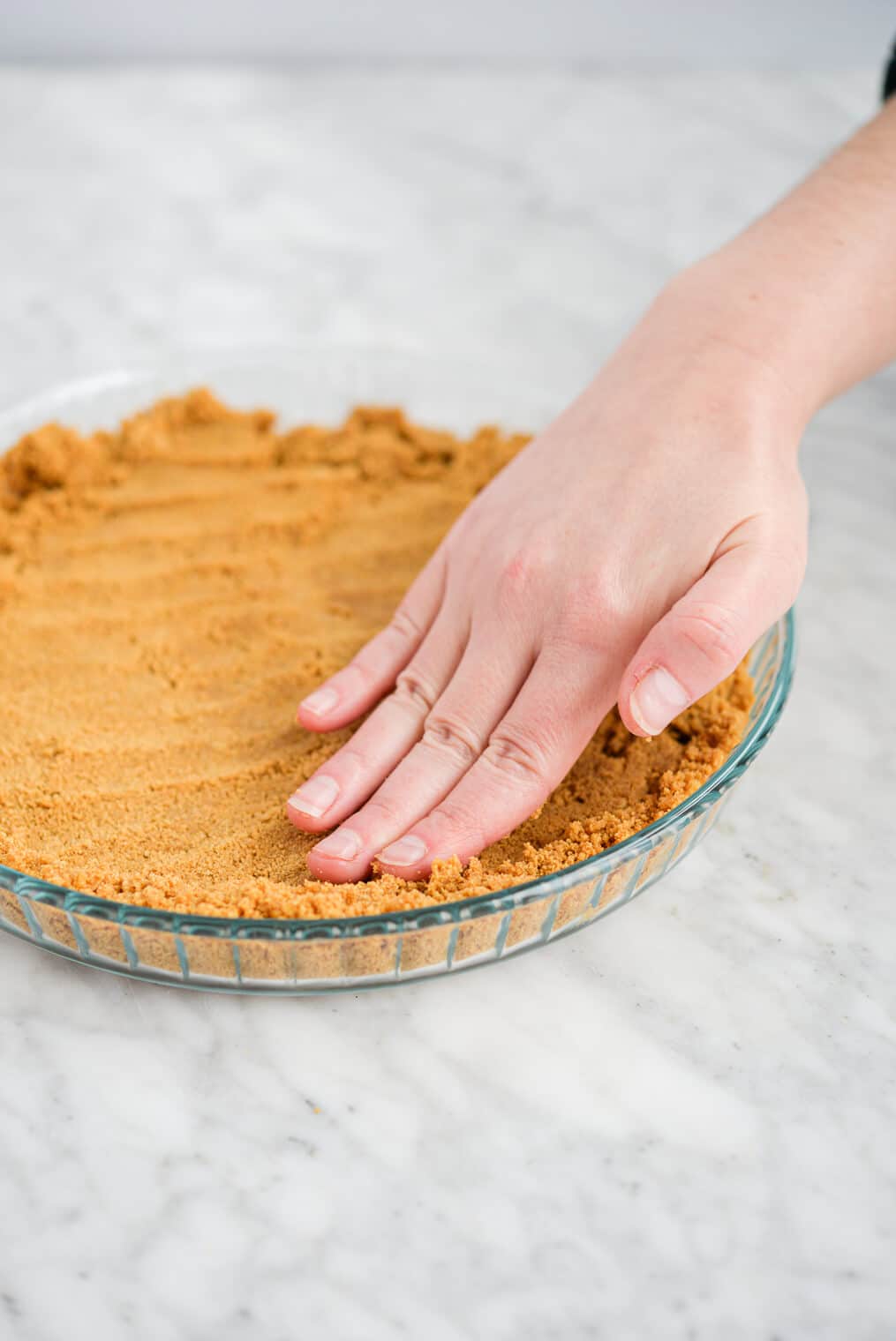 graham cracker crust crumbles being pressed into a clear glass pie plate