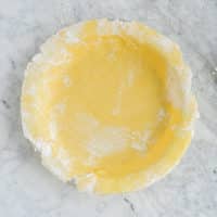 an uncooked, floured pie crust pressed into a pie pan sitting on a marble surface