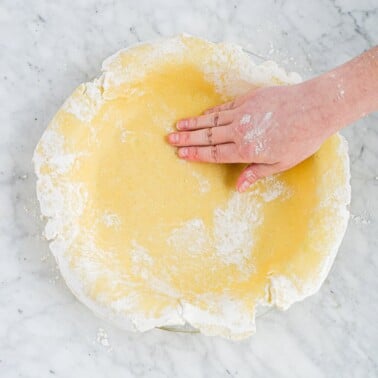 a rolled out pie crust being pressed into a pie pan