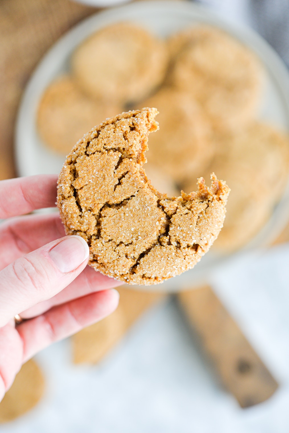 a woman's hand holding a ginger molasses cookie with a bite taken out of it