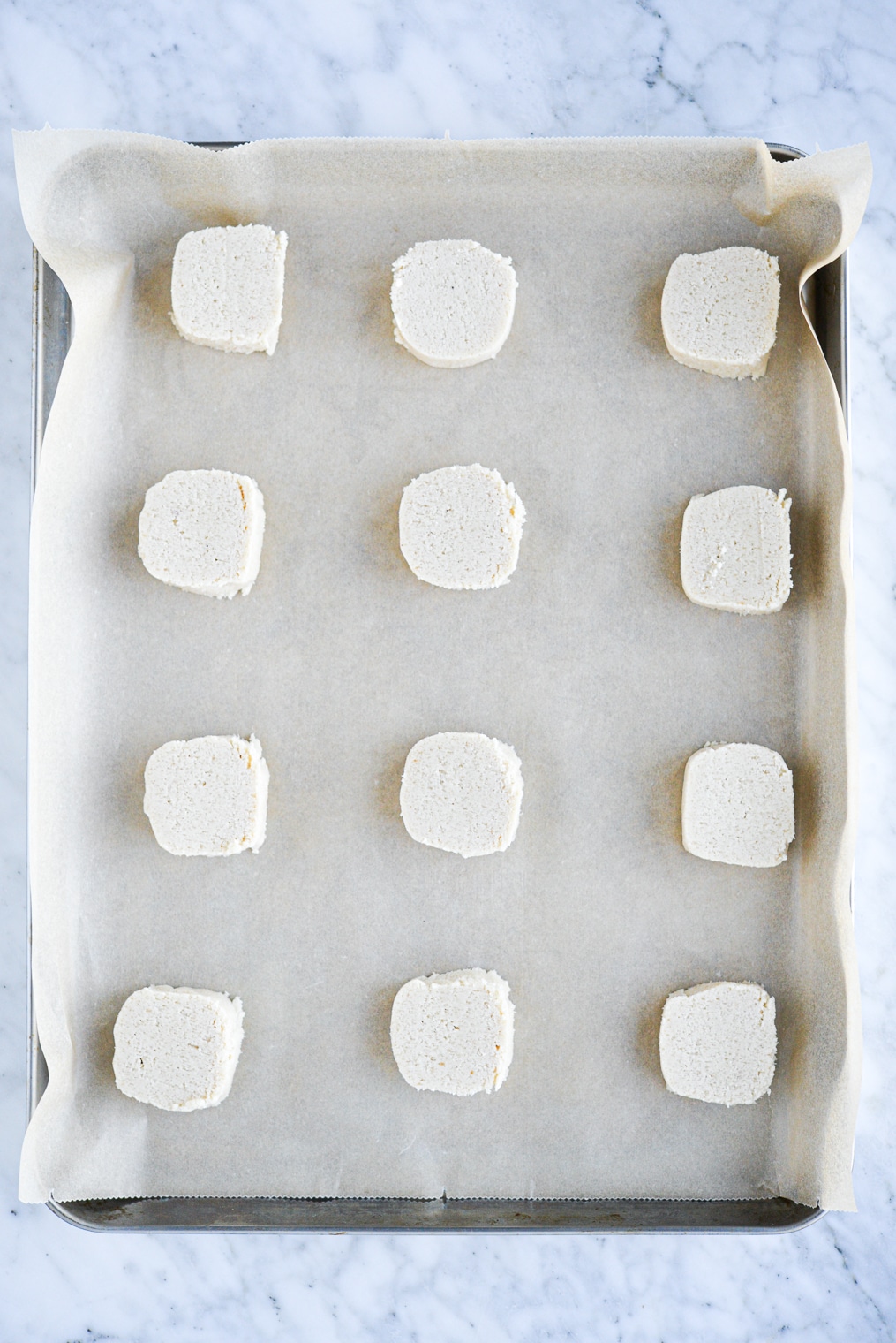 slices of cookie dough arranged on a parchment paper lined baking sheet on a marble surface