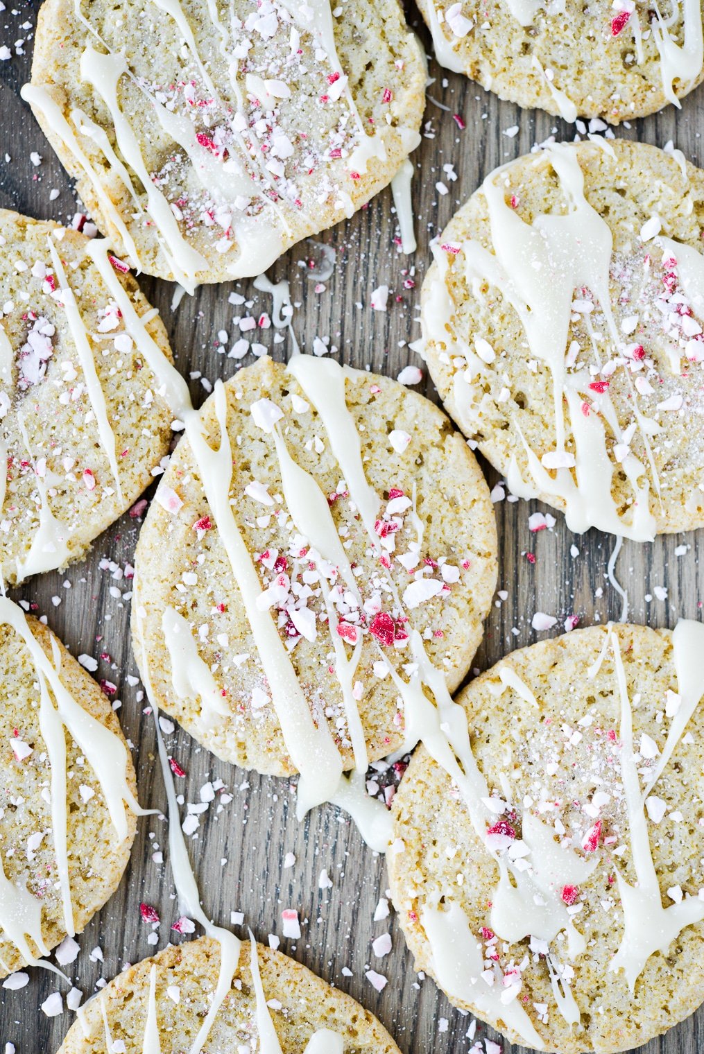 white chocolate peppermint cookies drizzled with white chocolate and crushed peppermint on a wooden surface