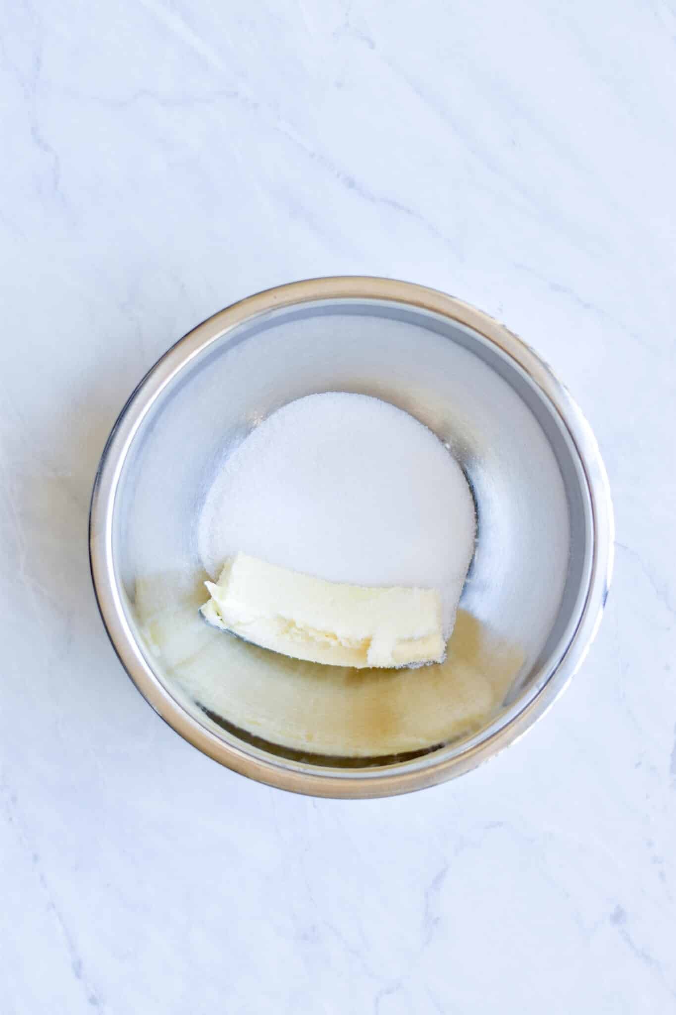 metal bowl on a marble surface filled with a stick of softened butter and sugar