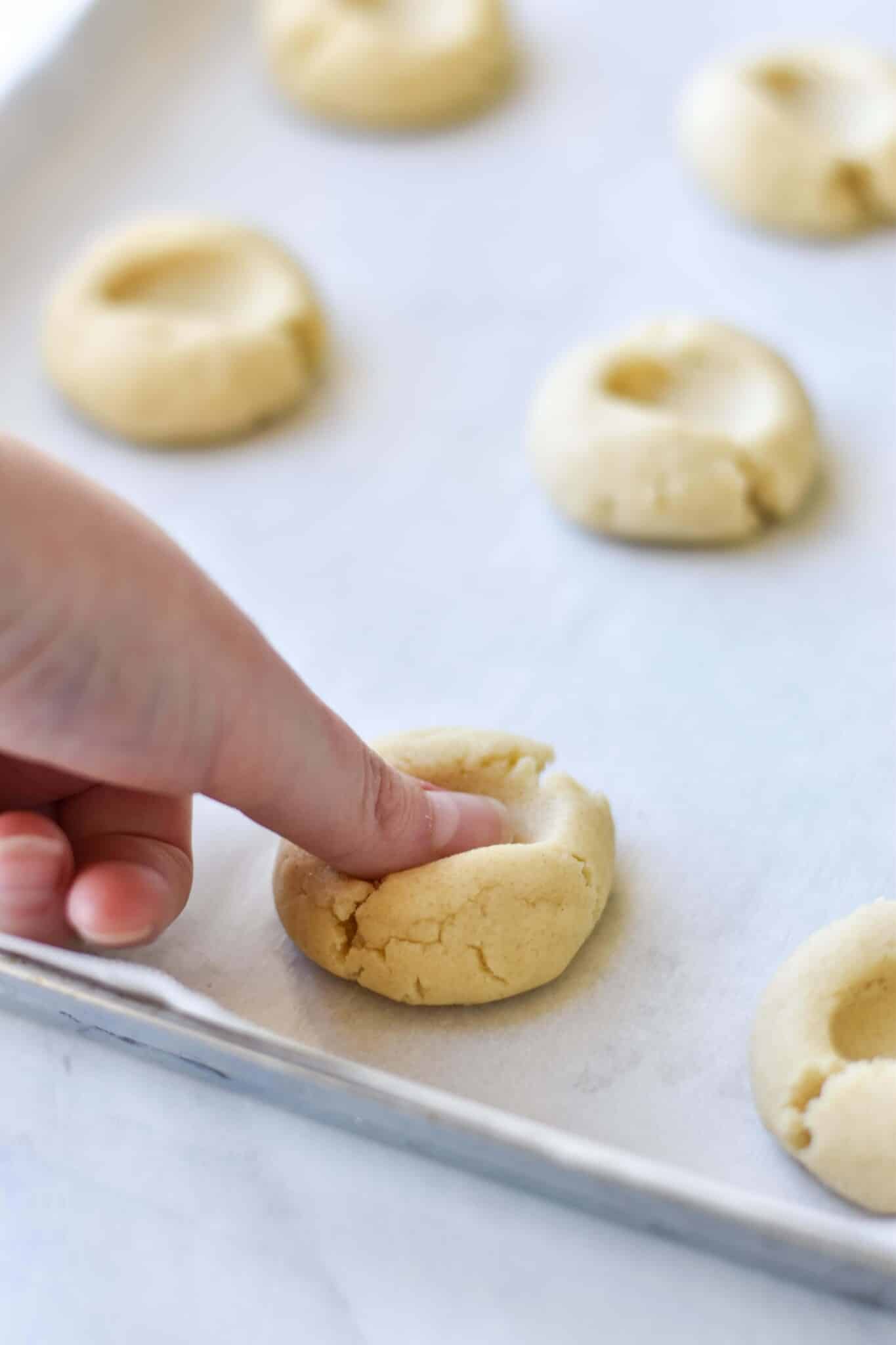woman's thumb pressing into a ball of cookie dough to make an indentation