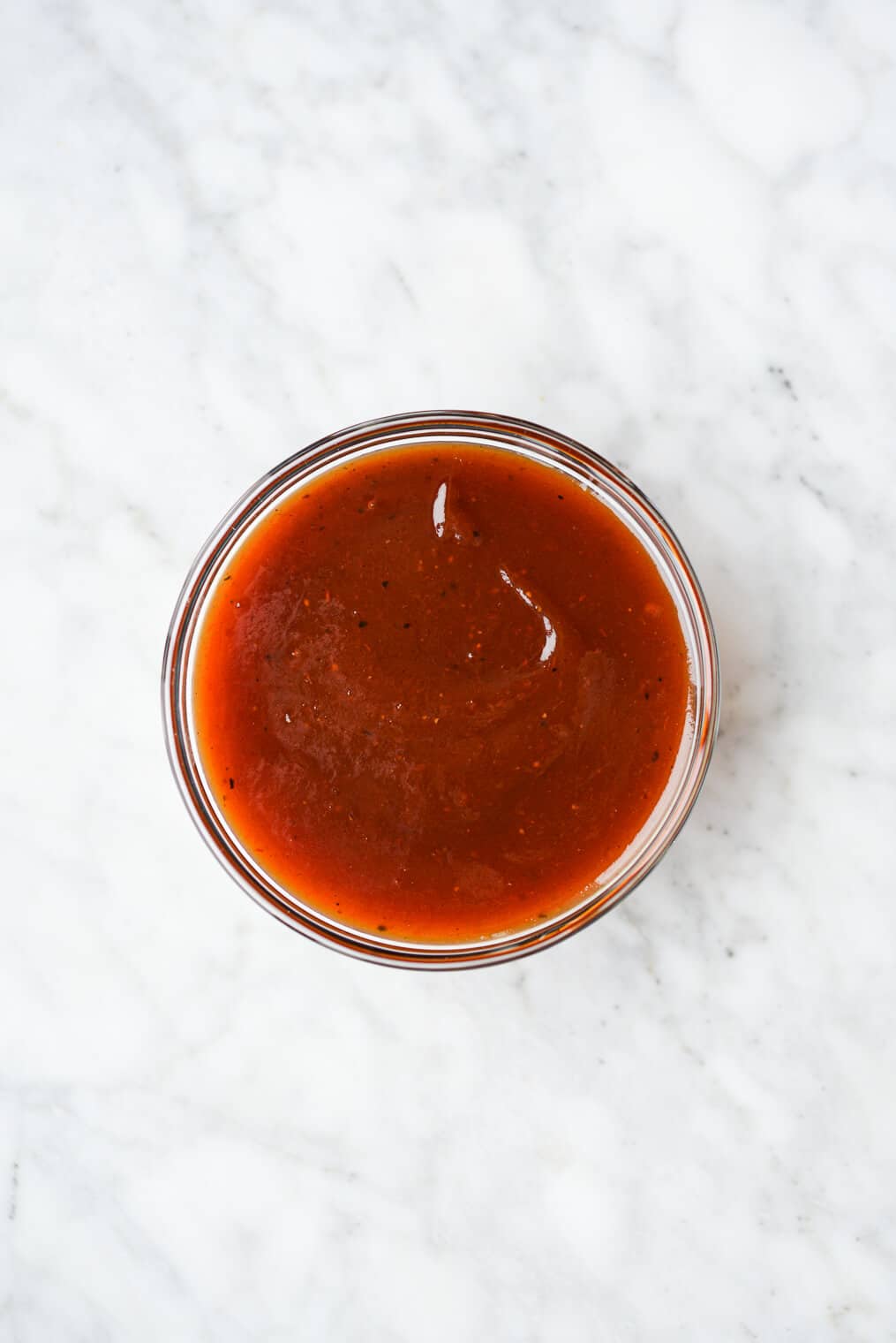 a small bowl of BBQ sauce sitting on a marble surface