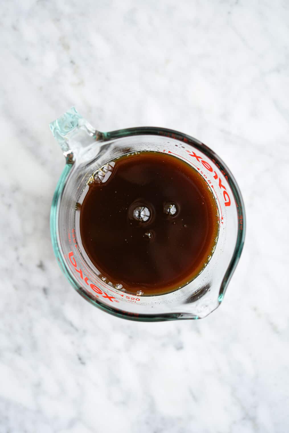 a glass measuring cup of teriyaki marinade sitting on a marble surface