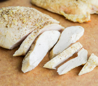 two baked chicken breasts (one sliced and one left whole) sitting on a cutting board next to a knife