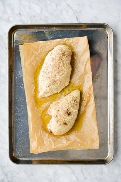 two seasoned and baked chicken breasts sitting on a parchment paper lined baking sheet