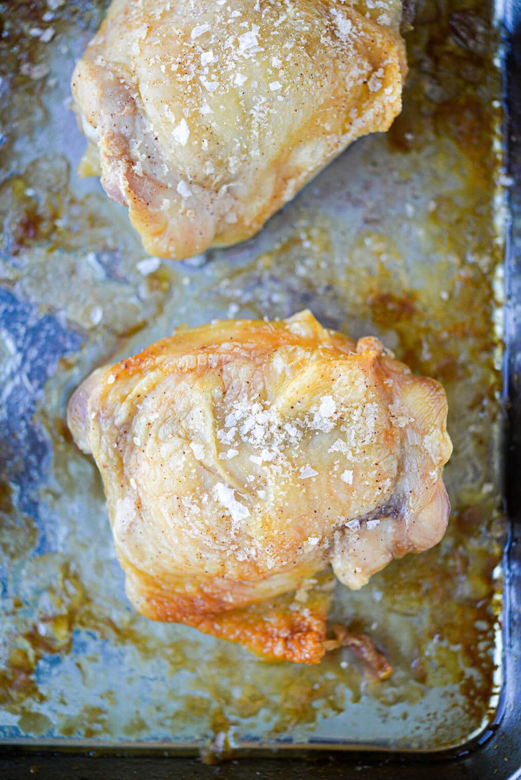 golden brown oven baked crispy chicken thighs on a stainless rimmed sheet pan sitting on a marble surface
