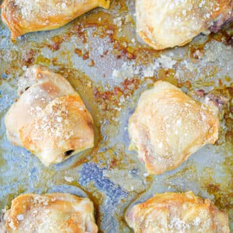 golden brown oven baked crispy chicken thighs on a stainless rimmed sheet pan sitting on a marble surface