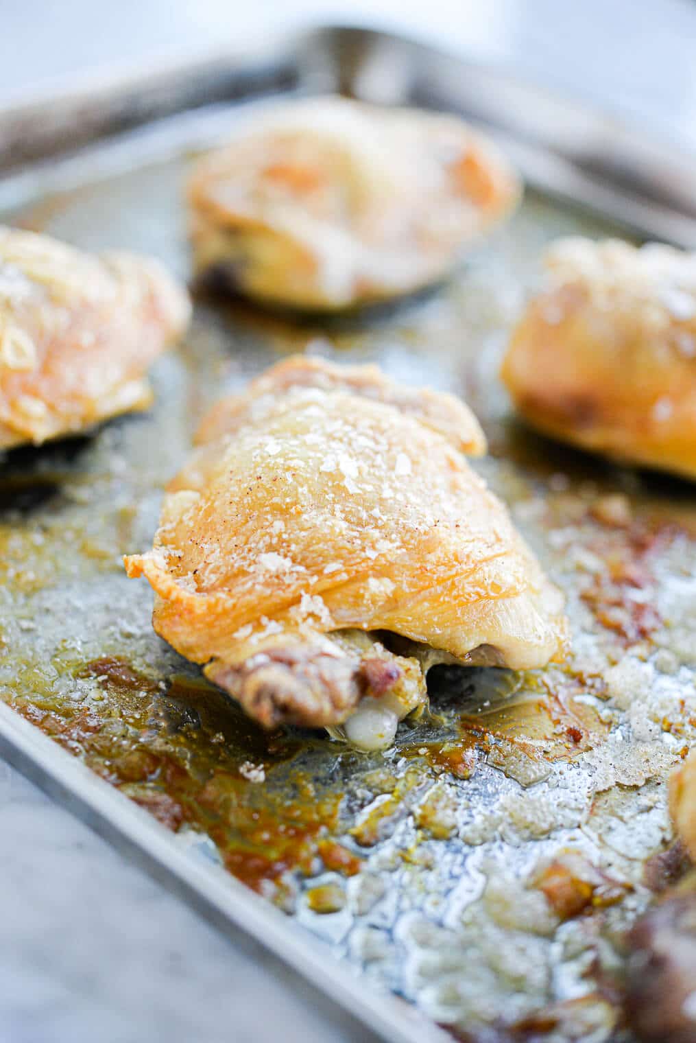 golden brown oven baked crispy chicken thighs on a stainless rimmed sheet pan sitting on a marble surface