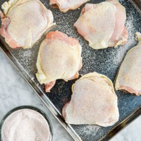 bone-in, skin-on chicken thighs that have been dry brined with sea salt laying on a stainless steel rimmed baking sheet