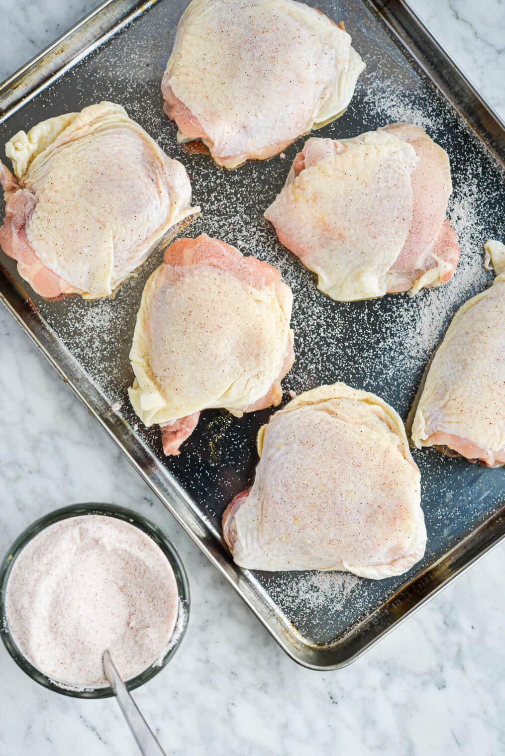 bone-in, skin-on chicken thighs that have been dry brined with sea salt laying on a stainless steel rimmed baking sheet