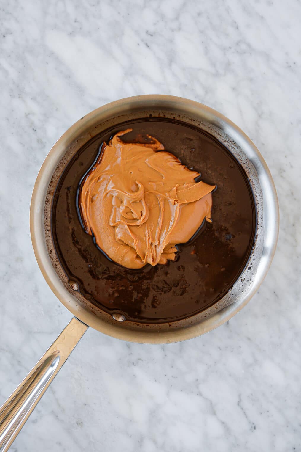 a stainless steel pan with a chocolate mixture with a dollop of peanut butter on top sitting on a marble surface