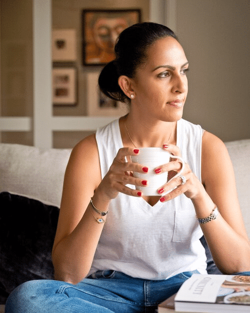 Riyana Rupani of Healthyish and Happy holding a coffee cup sitting on a couch looking off to the side