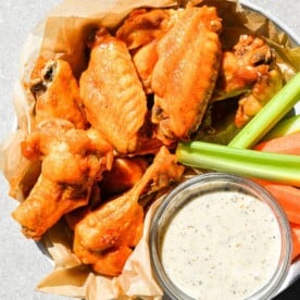 a bowl filled with Instant Pot buffalo chicken wings, carrots, celery, and a small dish of ranch dressing sitting on a gray background