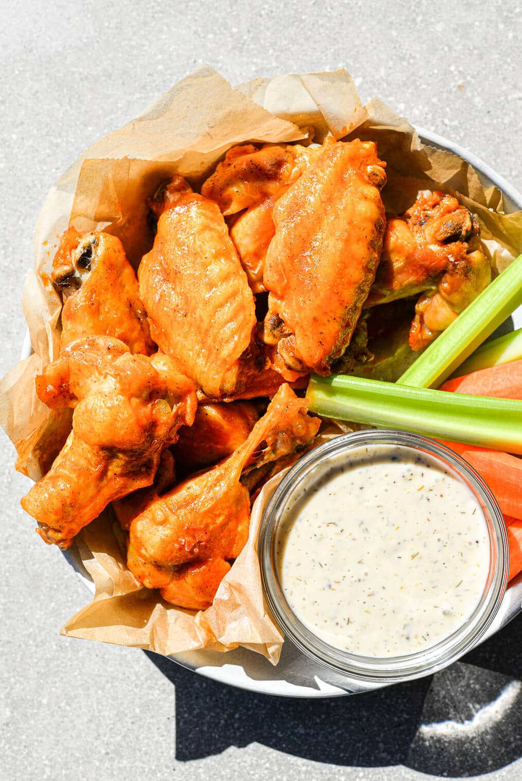 a bowl filled with Instant Pot buffalo chicken wings, carrots, celery, and a small dish of ranch dressing sitting on a gray background