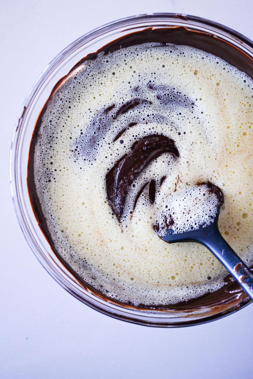 frothy whisked eggs being stirred into a bowl of melted dark chocolate