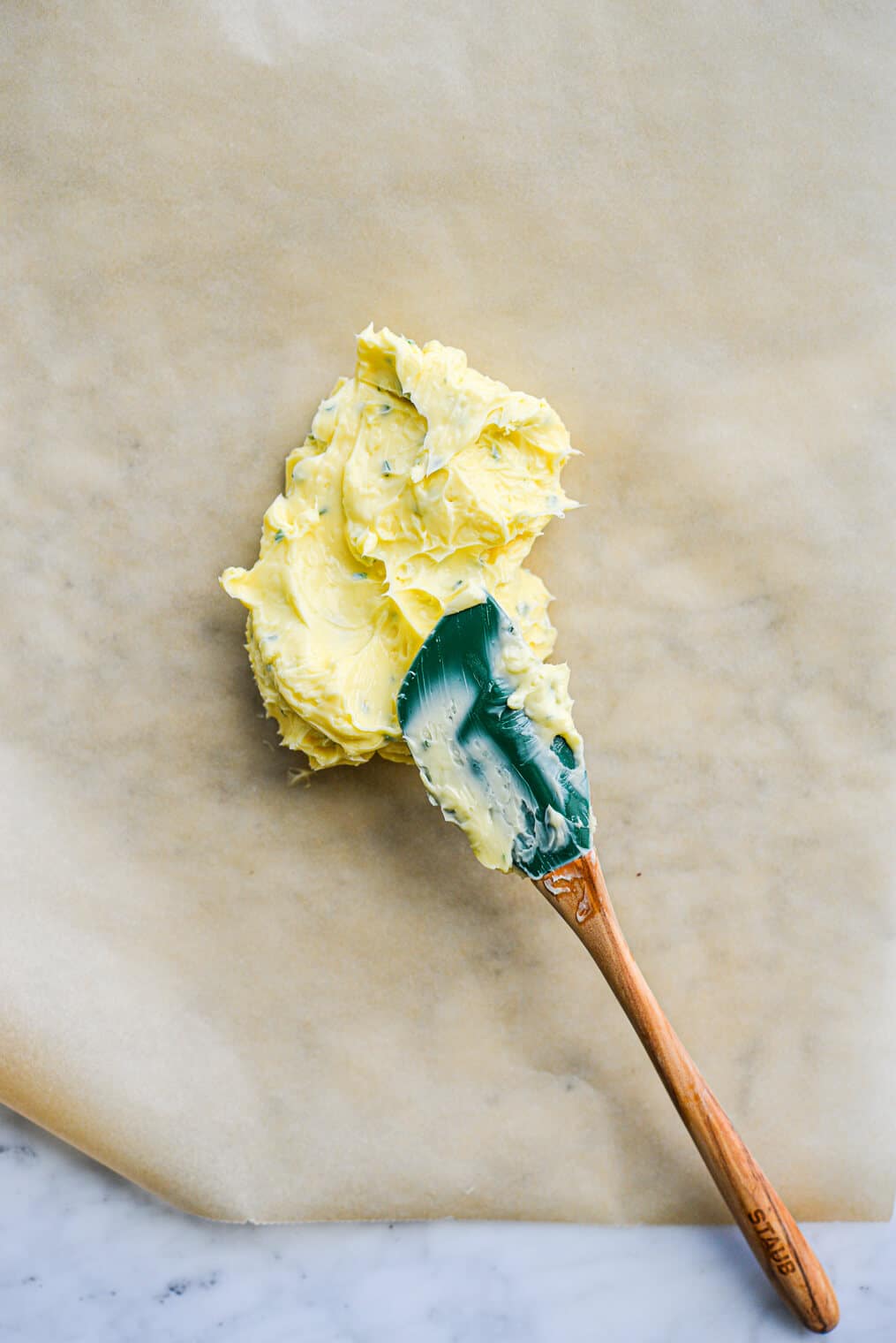 a spatula laying on top of a glob of compound garlic and herb butter sitting on a sheet of parchment paper