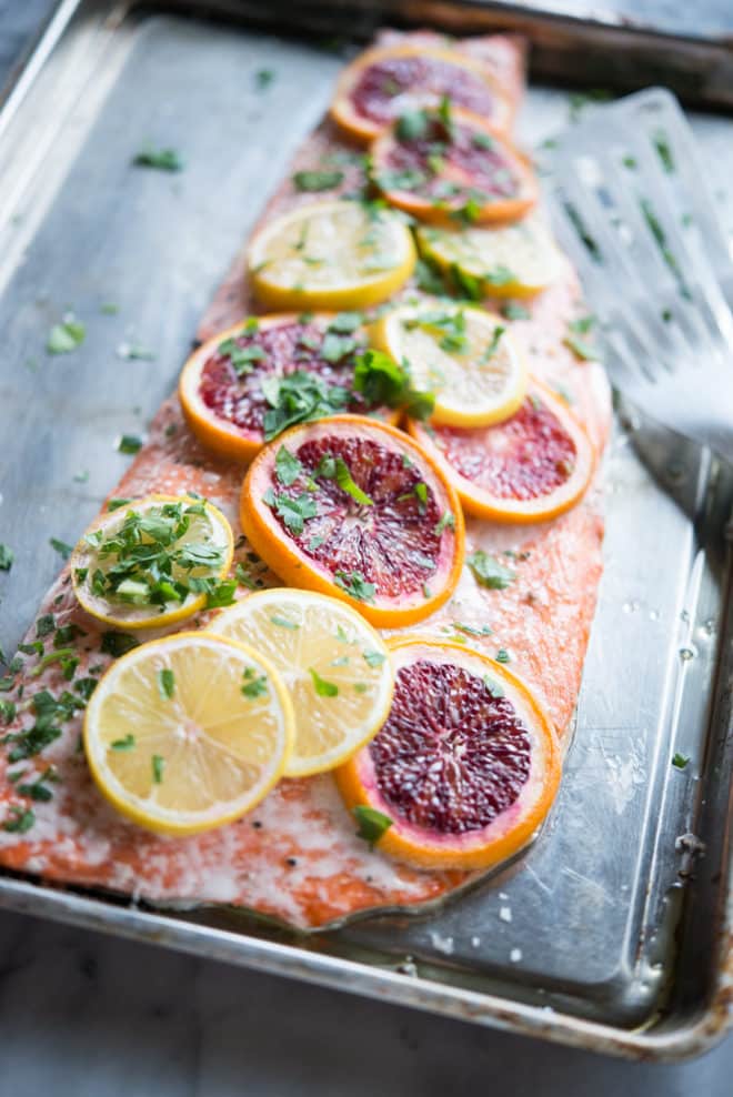 side view of a filet of citrus roasted salmon with thinly sliced blood oranges and lemons laying over top