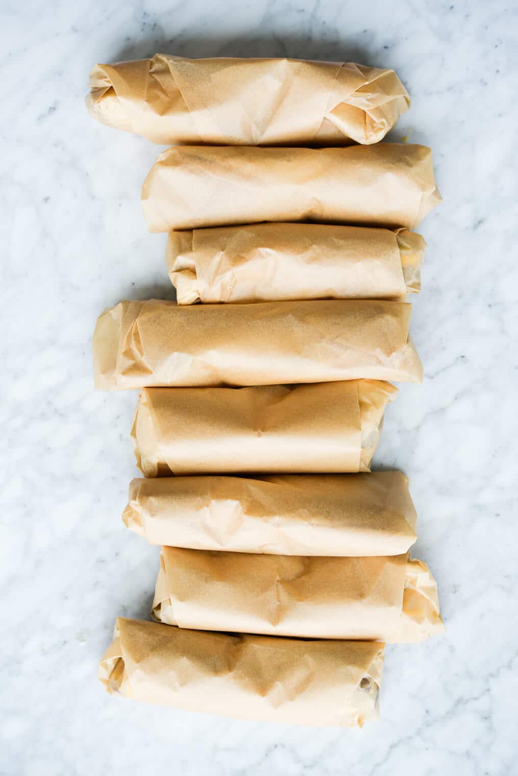 8 breakfast burritos rolled in parchment paper laying on a marble surface