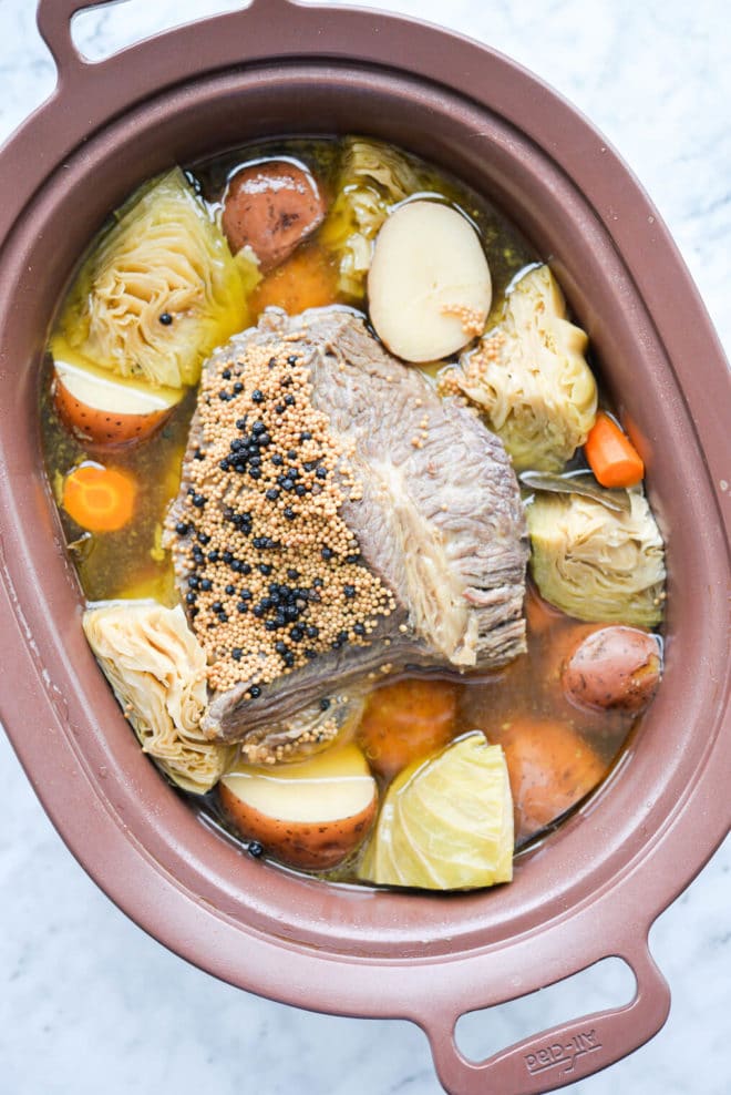 a slow cooker filled with cooked corned beef, cabbage wedges, carrots, and red potatoes.