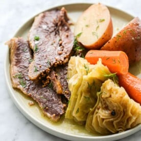 a plate of sliced corned beef, halved potatoes, carrots, and cabbage wedges sitting on a marble surface