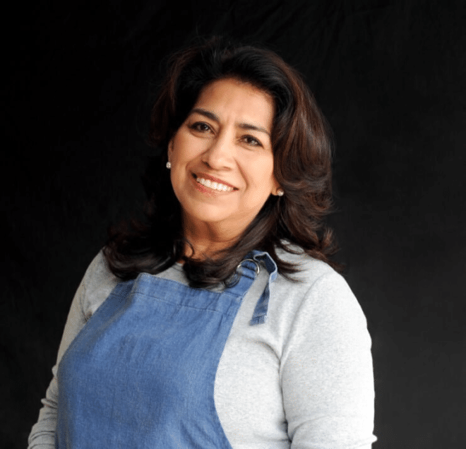 Mely Martinez of Mexico in My Kitchen standing in front of a black background with a denim apron on smiling at the camera