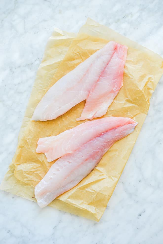 two raw filets of red snapper on parchment paper on a marble surface